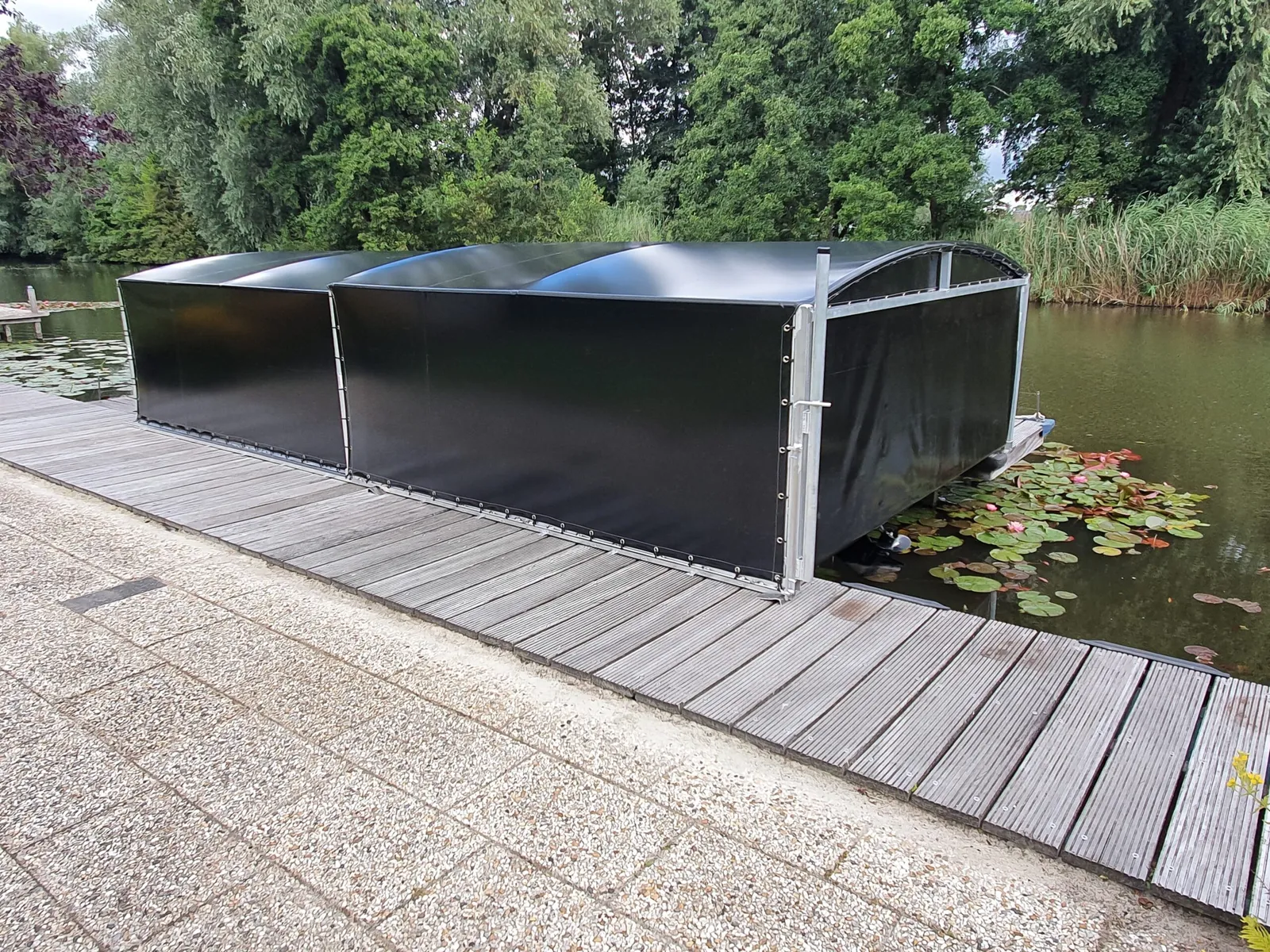 Gesloten zwarte bootoverkapping aan een steiger langs een waterpartij